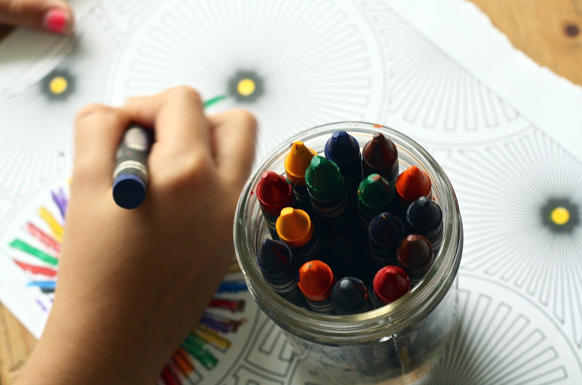 Photo of a child coloring with a jar of crayons nearby.