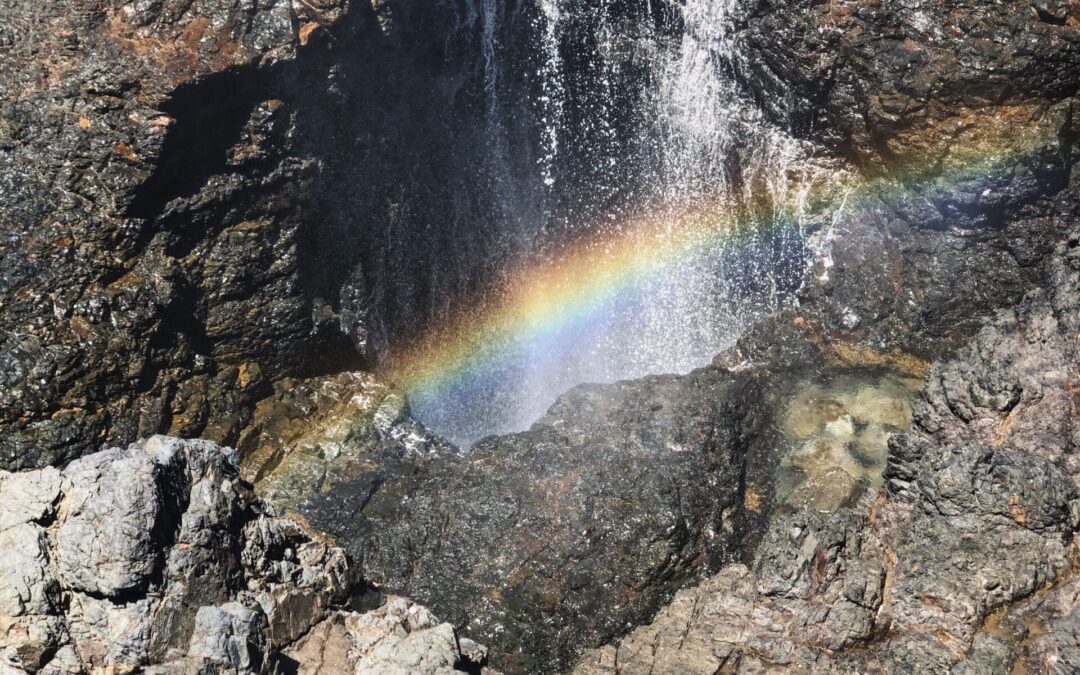 Picture of a rainbow cast by a waterfall on a rocky cliff